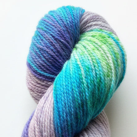 A twisted skein of variegated yarn with shades of blue, purple, green, and lavender, resting on a wooden surface.