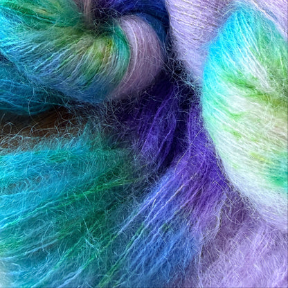 Close-up of soft, fluffy yarn or fiber strands in a variegated pastel mix of purple, blue, teal, green, and white.