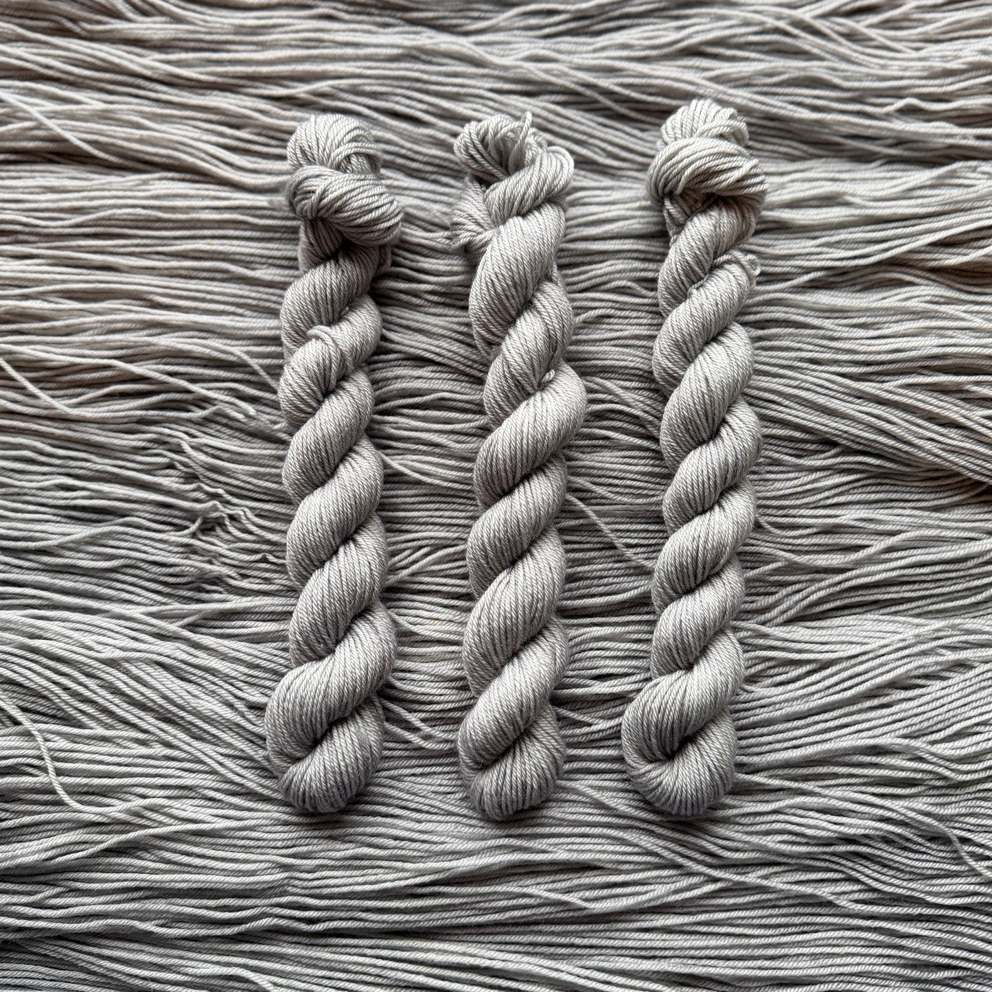 Three skeins of gray yarn on a textured yarn background
