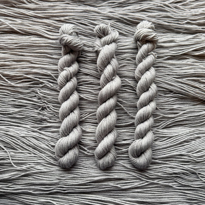 Three skeins of gray yarn on a textured yarn background