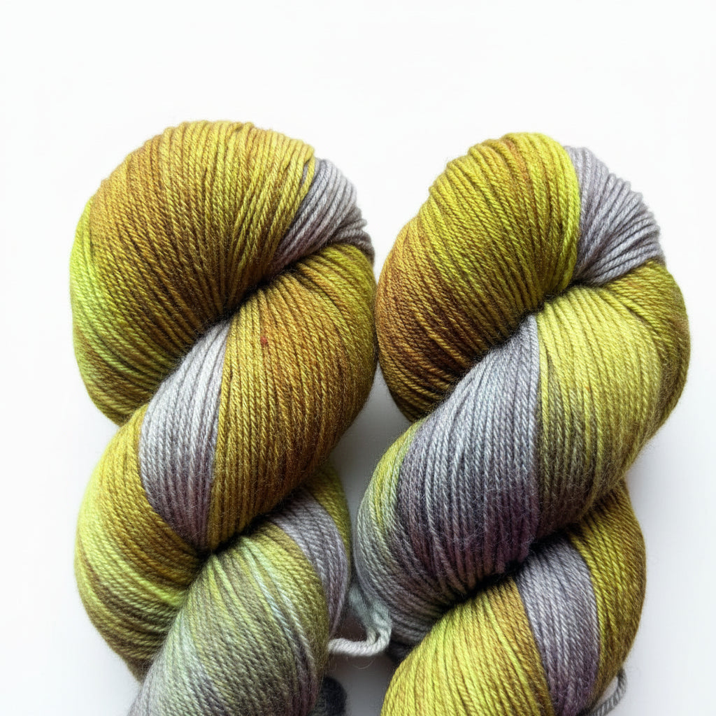 Two hanks of variegated yarn on a wooden surface, featuring stripes of olive green, mustard yellow, and muted gray