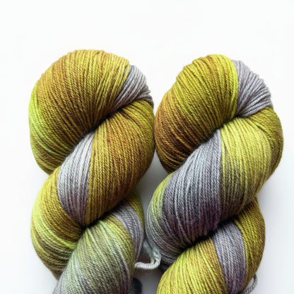 Two hanks of variegated yarn on a wooden surface, featuring stripes of olive green, mustard yellow, and muted gray
