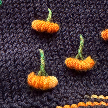 Pumpkin Patch Noir assigned pooling yarn, detail view of the pumpkin motif on black